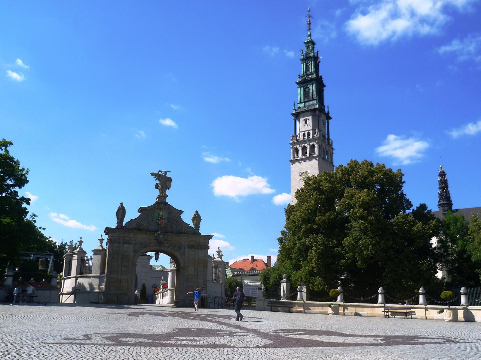 Barokowa Brama Lubomirskich i wysoka wieża bazyliki jasnogórskiej na tle błękitnego nieba z obłokami.